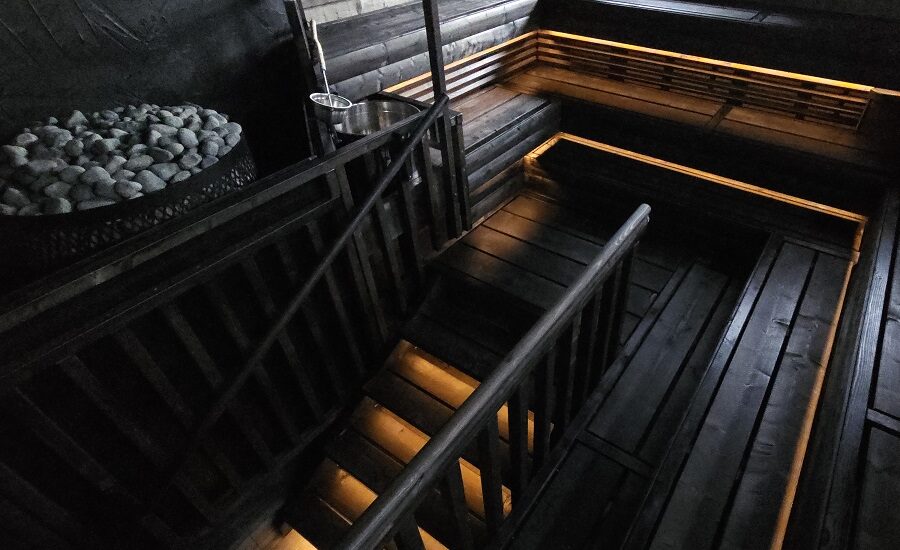 Sauna lighting using LED strips in aluminum profiles under the bench surfaces and stair steps, with a warm white light tone.